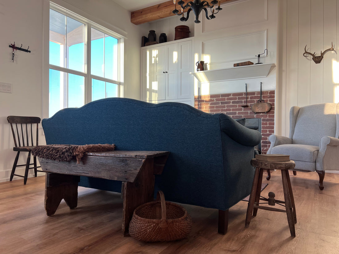 Early American style keeping room with blue sofa and rustic wood bench holding. 